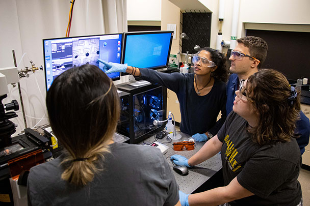 four students gathered around a computer monitor in a lab