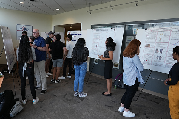Students and faculty gather in conversation in front of research posters displayed around a room