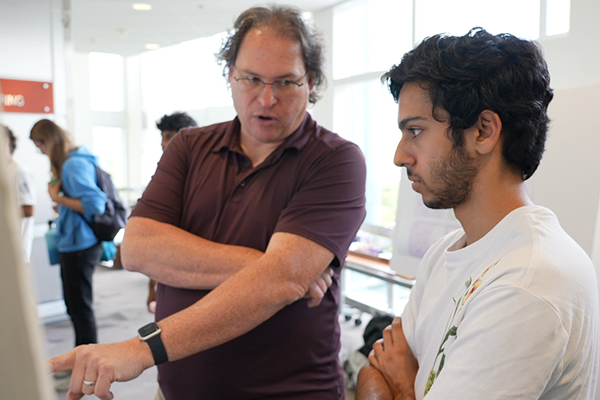 A professor points at a research poster while talking to a student