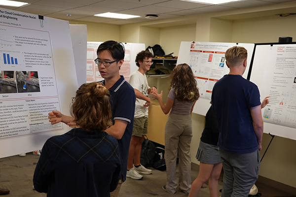 Students cluster around three research posters in a room