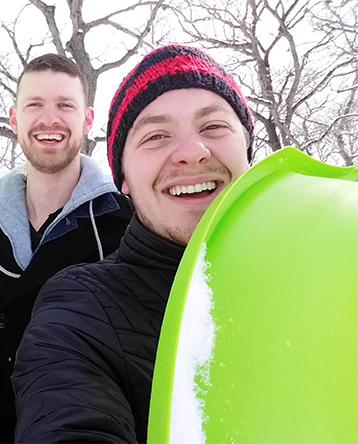 Nicholas Lamson outside in the snow holding a neon green sled