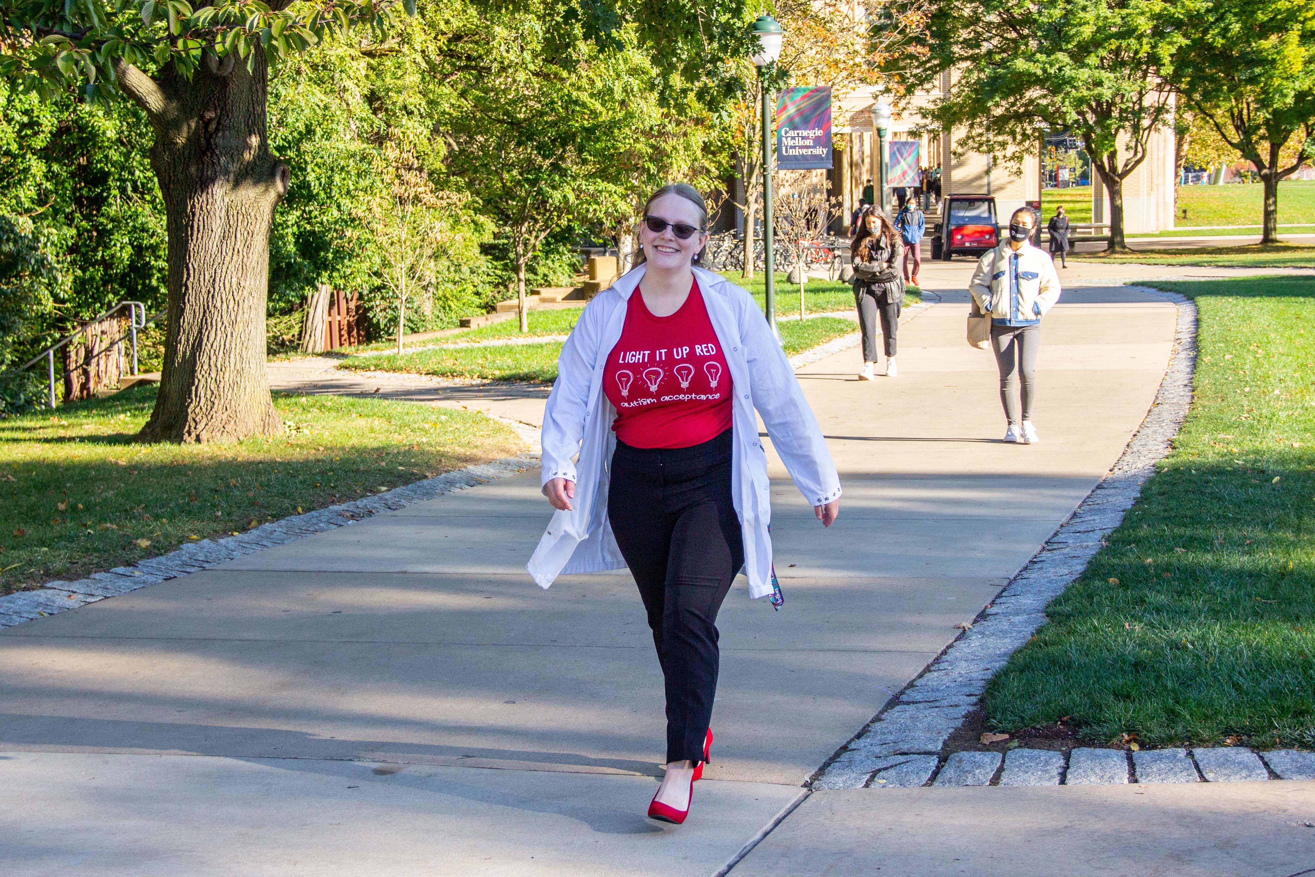 Arral walks down sidewalk at CMU wearing "Light it up Red for Autism" shirt