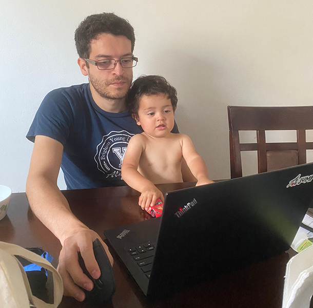 Hector Perez working at his laptop with one of his children sitting on his lap