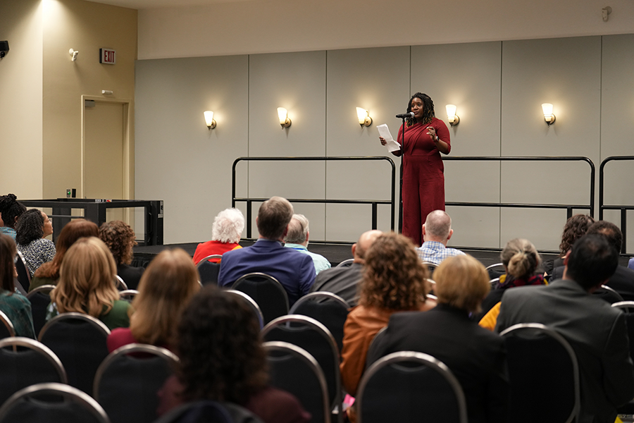 Liz Wayne speaking from a stage to a seated audience in a function room.