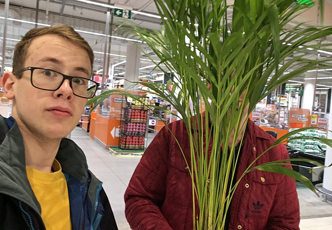 Daniil Boiko stands in a store, next to a person obscured by the palm plant they are holding