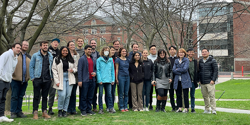 A group of adults pose for a photo outside on a college campus.