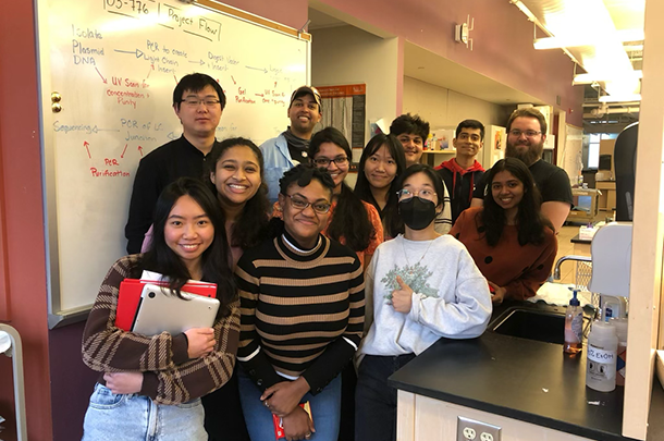 A group of graduate students posed for a photo next to a whiteboard with a project flow chart.