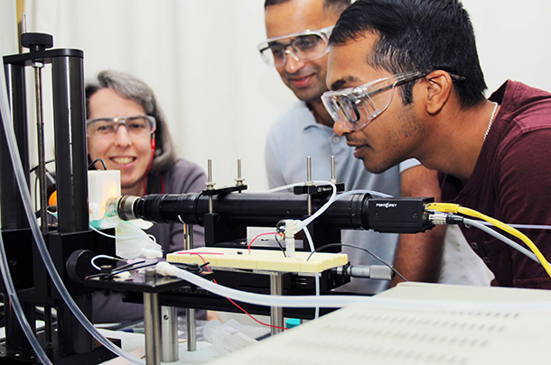 Three adults bending down to look closely at laboratory equipment