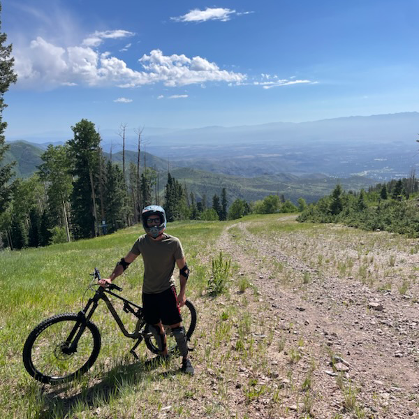 Sergio Bugosen wearing a helmet, standing next to his mountain bike on the side of a mountain trail