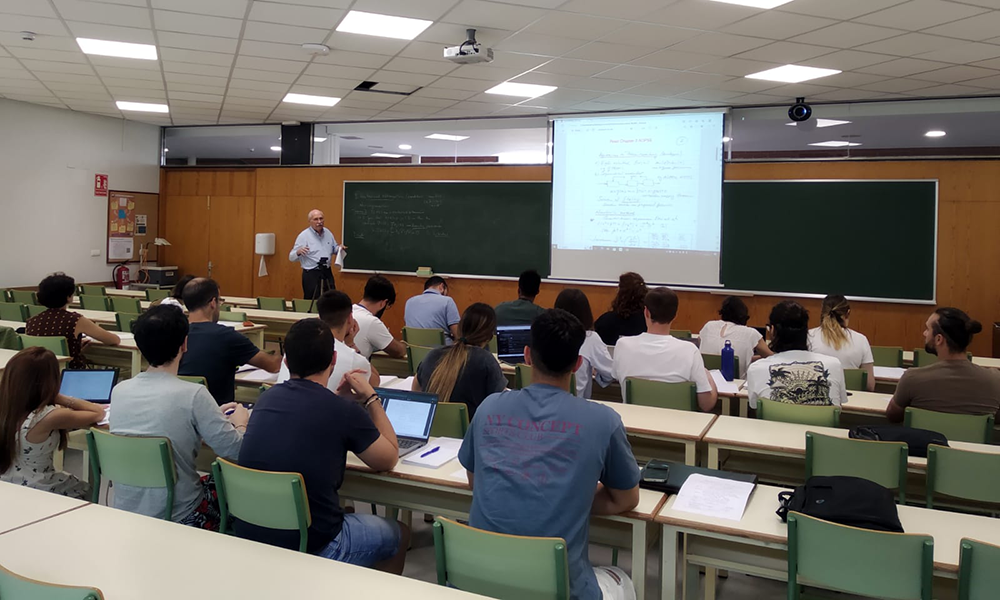 Ignacio Grossmann standing in front of a projection screen teaching a classroom full of students seated at rows of tables.