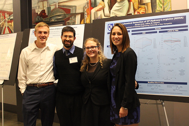 Four adults standing in front of research posters and smiling