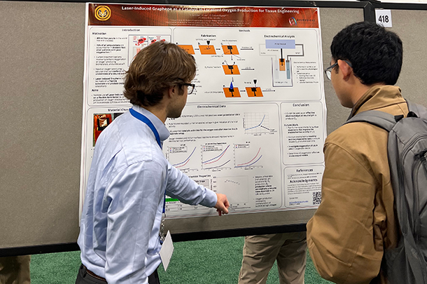 Two students stand looking at a research poster