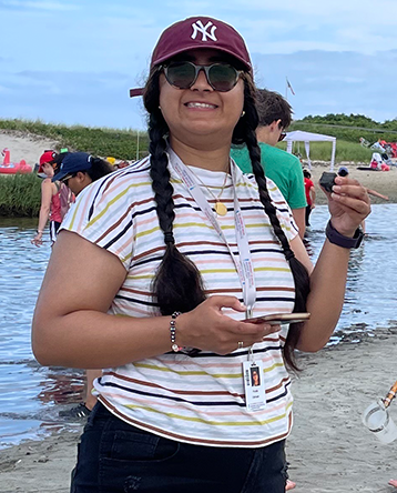 Huda Usman stands on a beach holding a sand sample 