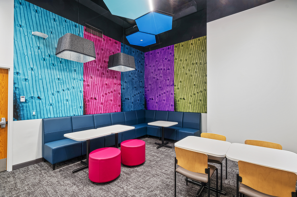  Lounge area with blue banquette, pink ottomans, tables, chairs, and wall art in blue, green, pink, and purple.