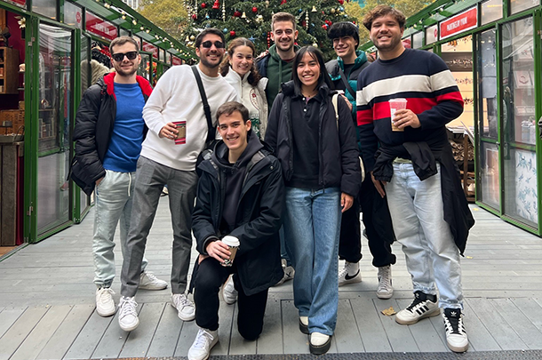 A group of 8 young adults poses for a photo in front of a large Christmas tree