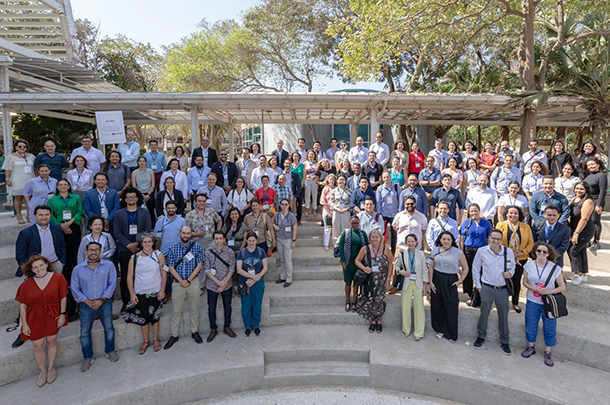 A group of around 90 adults stands on stone steps outside, posing for a group photo.