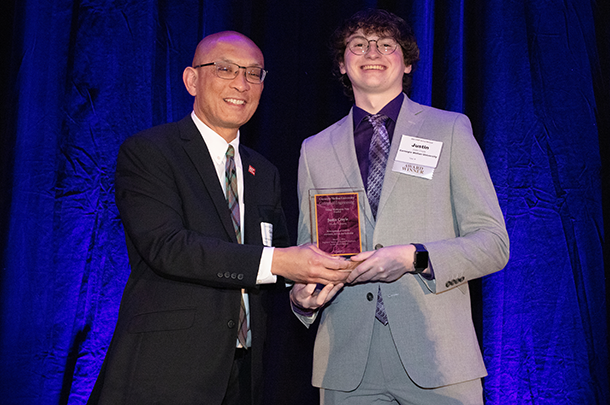 Conrad Zapanta and Justin Croyle stand in front of a blue backdrop holding an award plaque