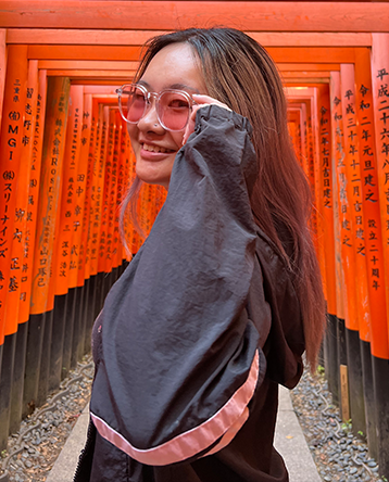 Vicki Huang turns back to smile at the camera while standing under red wooden arches with Japanese inscriptions.