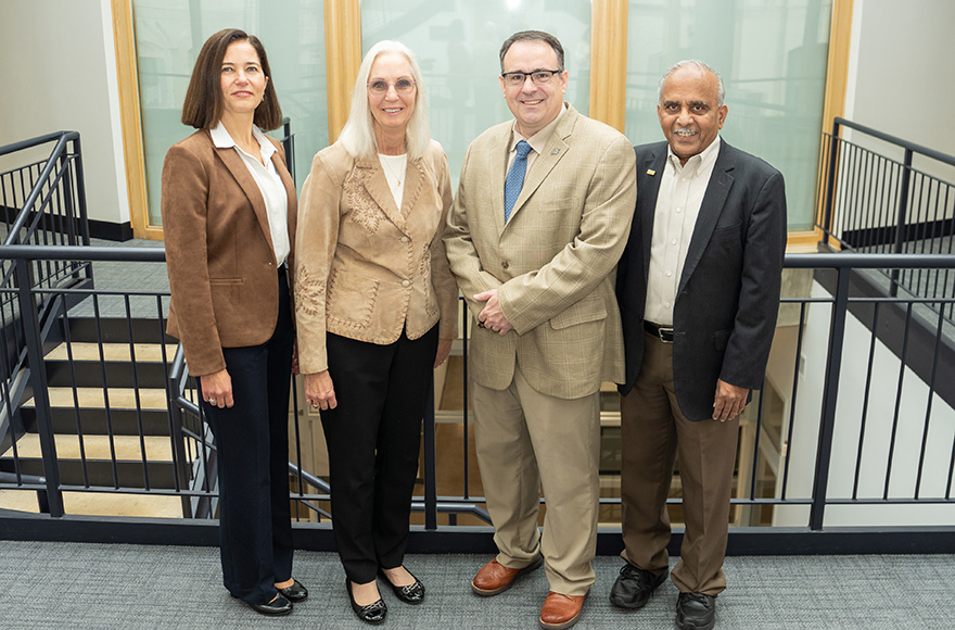 Four adults wearing suits stand for a photo.