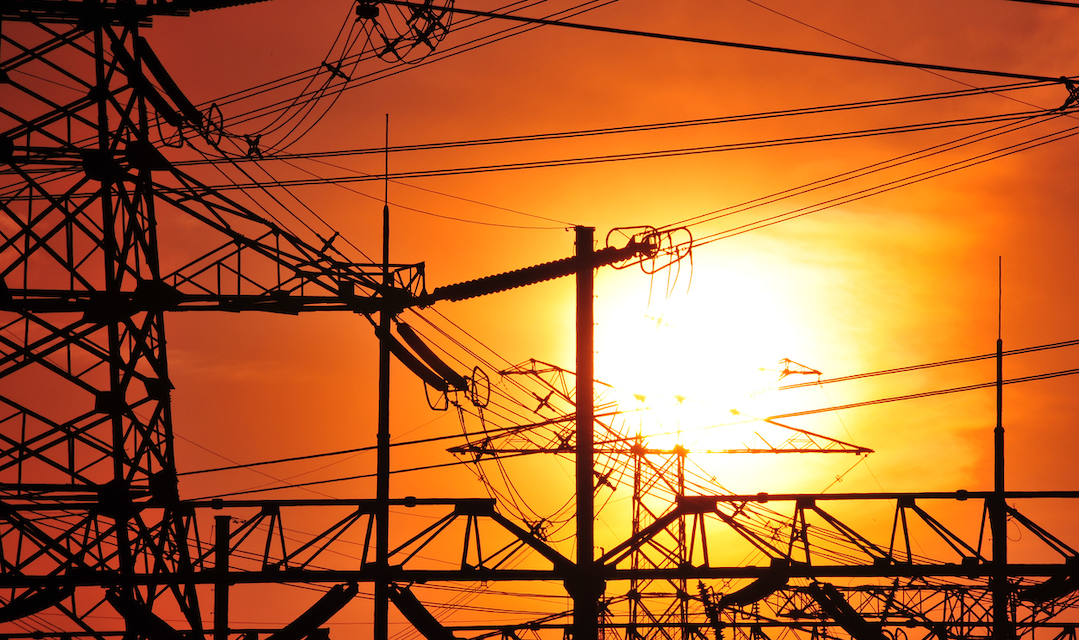 A yellow sun is shining against an orange sky with electrical pylons and wires in the forefront.