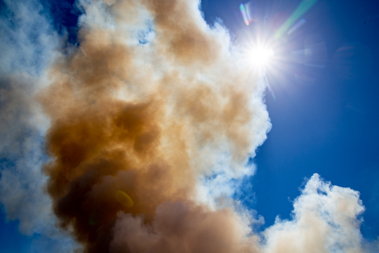 Image of brown smoke clouds mixing with white clouds against a bright blue sky with the sun visible